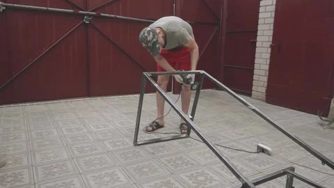 A man in a working uniform processes a metal frame with a drill Vidéo 145182235