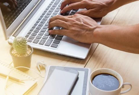 A man is working by using a laptop computer on wooden desk. Stock Photos