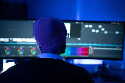 Man working on video editing in a dimly lit room with dual monitors display.. Stock Photos