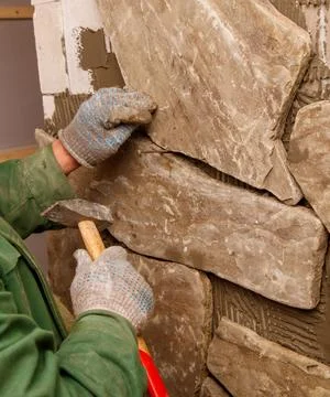 A man is working on a wall, using a hammer and chisel to shape a stone Stock Photos