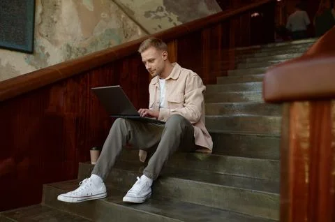 Man working on wireless laptop computer sitting on stairs in office Foto stock