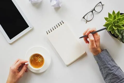 Man working writing in the notepad and drinking coffee at his workplace Stock Photos