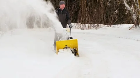 A man is working with a yellow snowplow, clearing the driveway Stock Footage 299789012