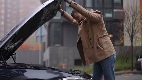 A man works on a car problem in a bustling urban city, immersed in a vibrant Stock Footage 314763275