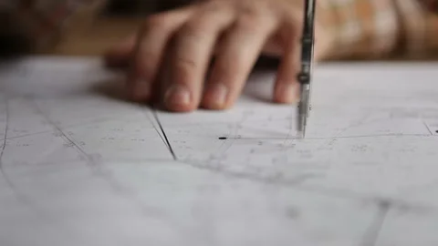 A man works with a compass and drawings while sitting at a table. Macro Stock Footage 266106097