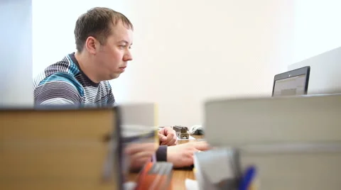 Man works at the computer in the background of books and magazines Vidéo 63079549