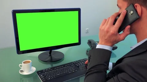 A man works on a computer with a green screen and talk on a smartphone in an 스톡 동영상 72002773