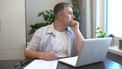 A man works at a computer, then thinks and looks out the window Stock Footage 282441674