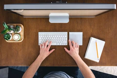 A man works at a computer, top view. Desktop computer on a wooden table. Stock Photos