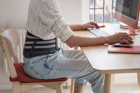 Man works on computer wears back support belt on lower back to relieve stress on Stock Photos