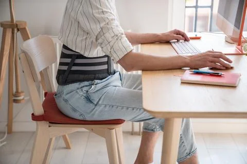Man works on computer wears back support belt on lower back to relieve stress on 스톡 사진