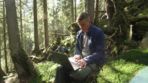 A man works at a computer while hiking in the mountains in the forest. Stock Footage 213015399