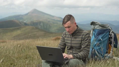A man works at a computer while hiking in the mountains. Stock Footage 214329482