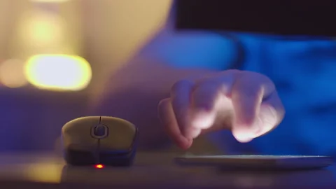 A man works in the evening at a computer through a computer mouse and answers Stock Footage 154184423