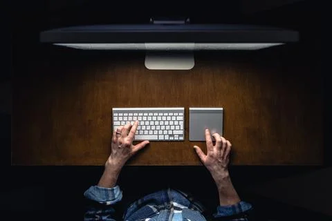 A man works in front of a computer at night, top view. Stock Photos