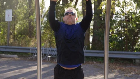 A man works hard to cross the monkey bars at an outdoor exercise park - slow Stock Footage 123489178