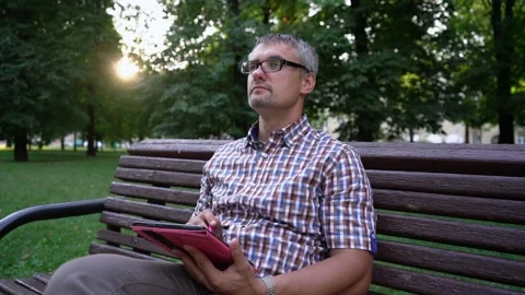 Man works hard on tablet sitting on bench in city park Vidéo 162908402