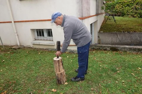 A man works in his backyard using a hammer and chisel to split wood Stock Photos