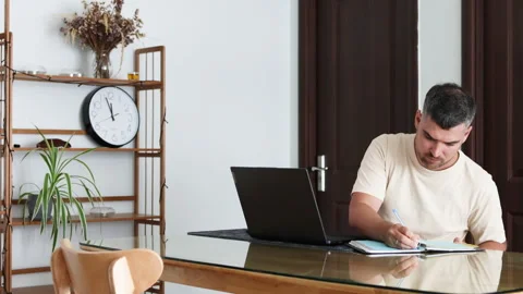 A man works on his laptop while making notes in a daily planner. Video stock 310526551