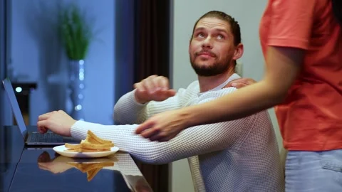 A man works at home at a computer in the middle plan, a woman brings him a plate Видео 267417631