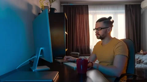 A man works at home at a computer while drinking a drink from a cup, time lapse Stock Footage 233546493