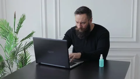Man works at home at a laptop and disinfects his hands Stock Footage