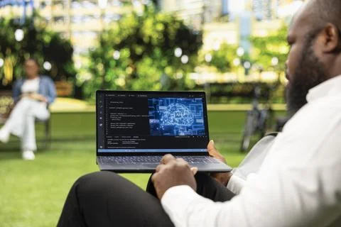 Man works on laptop displaying source code and digital AI interface Stock Photos