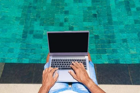 A man works on a laptop by the pool. View from above. Freelance. Stock Photos