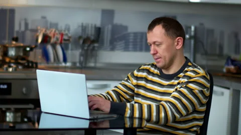 A man works at a laptop while sitting at home in the kitchen Video stock 131954383