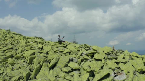 A man works on a laptop while sitting on top of a rocky mountain. Stock Footage 248202710