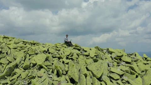 A man works on a laptop while sitting on top of a rocky mountain. Stock Footage 248202740