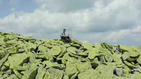 A man works on a laptop while sitting on top of a rocky mountain. Stock Footage 248203229