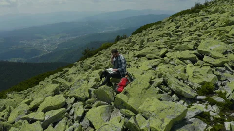 A man works on a laptop while sitting on top of a rocky mountain. Stock Footage 248203242