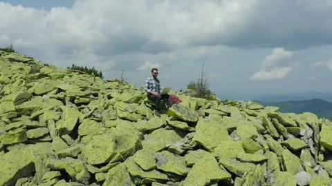 A man works on a laptop while sitting on top of a rocky mountain. Stock Footage 248203367