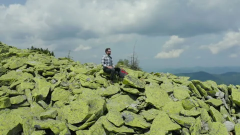 A man works on a laptop while sitting on top of a rocky mountain. Stock Footage 248203374