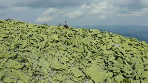 A man works on a laptop while sitting on top of a rocky mountain. Stock Footage 248203945