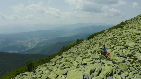 A man works on a laptop while sitting on top of a rocky mountain. Stock Footage 248204896