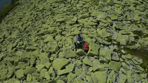 A man works on a laptop while sitting on top of a rocky mountain. Stock Footage 248205876