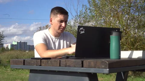 A man works on a laptop while sitting on a bench outdoors. Work remotely Stock Footage 255928287