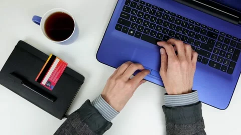 A man works with a laptop on a white table. Notepad, credit card, cup of tea Stock Footage 101752388