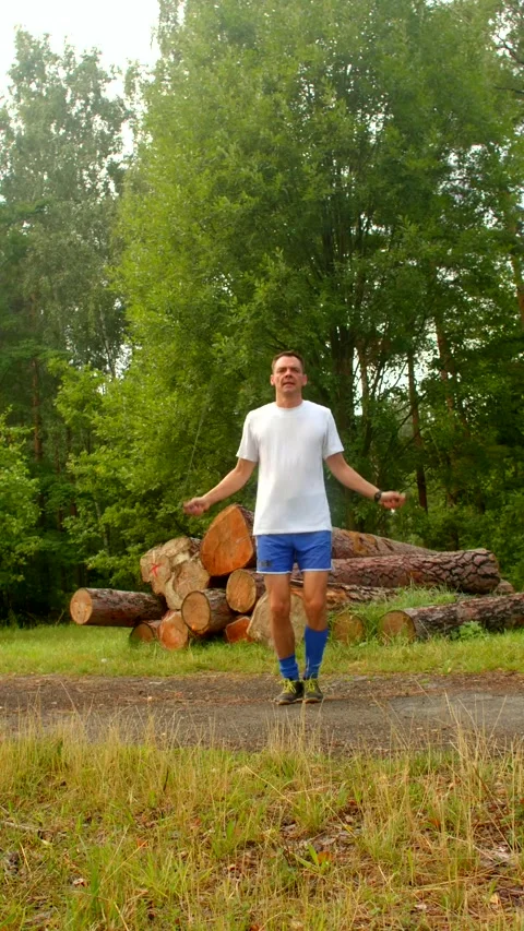 A man works out energetically, jumping rope before stacked logs Stock Footage 314346324