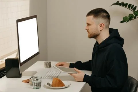 A man works remotely using a desktop computer holding a tablet computer at ho 스톡 사진