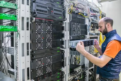 A man works in a server room. System administrator installs a new server in a Stock Photos