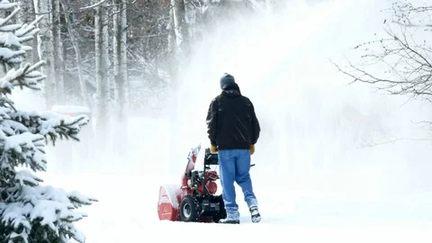 Man works with a snow blower to remove newly fallen snow from driveway. Stock Footage 103342338