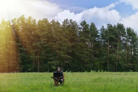 A man works at a table with a laptop in an empty field. Remote work in the field Stock Photos