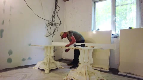 Man works on a table in a room with bare walls and wires hanging from the ceilin Stock Footage 340357293