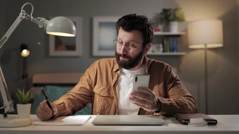 Man works using phone. Bearded freelancer in home office reading message, typing Vidéo 188729518