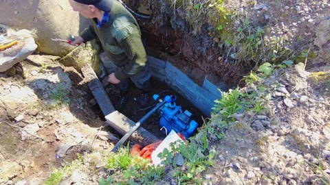 Man works on a water pump installation in a hole on a farm during daylight hours 스톡 동영상 337464790
