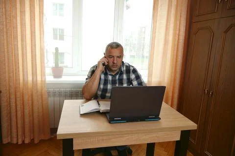 A man works while sitting at a table with a laptop. Stock Photos