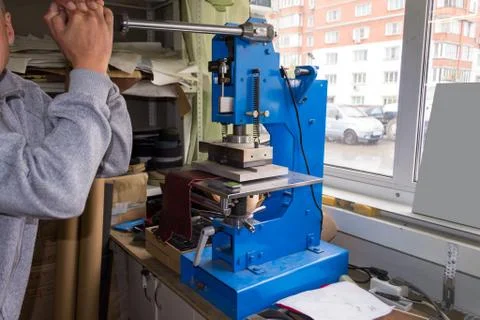 The man in the workshop presses the lever on the press machine to get the emb Stock Photos